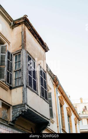 Verwitterte Wohnhausfassade mit Holzläden und veraltetem Putz vor klarem Himmel. Nikosia, Zypern. Stockfoto