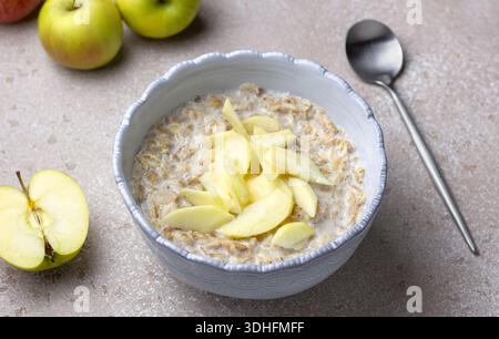 Mehrkornbrei aus Roggen, Hafer, Gerste, Buchweizen und Weizenflocken, serviert mit Milch und frischen Apfelscheiben. Neutraler Steinhintergrund Stockfoto