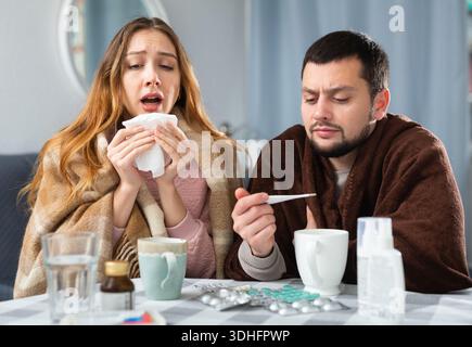 Frau und Mann in Plaids gehüllt mit Symptomen von Kälte zu Hause Stockfoto