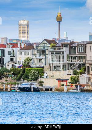 Häuser am Wasser des Hafens von Sydney mit der Skyline der Stadt dahinter Stockfoto