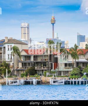 Häuser am Wasser des Hafens von Sydney mit der Skyline der Stadt dahinter Stockfoto