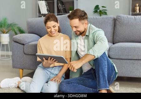 Glückliches Paar, das im gemütlichen Wohnzimmer lächelnd und stöbernd auf dem Boden sitzt Stockfoto