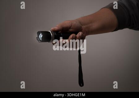 Eine Taschenlampe, die im Griff der rechten Hand mit dunkelgrauem Hintergrund aufleuchtet Stockfoto