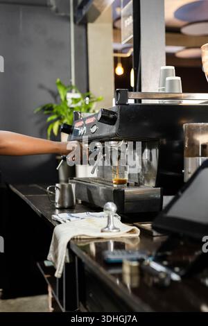 Die Espressomaschine gießt Espresso in ein Glas mit Milchkrug und Handtuch Stockfoto