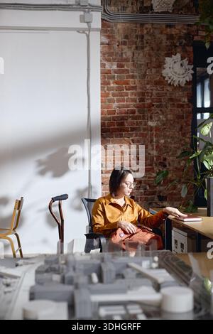 Kaukasische Frau mittleren Alters mit Behinderung sitzt am Schreibtisch Stockfoto