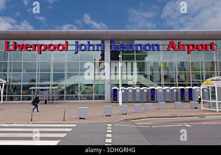 Äußere des Flughafenterminals Liverpool John Lennon mit auffälligen Schildern, Glasfassade, Fußgängerübergang und Vorplatz unter blauem Himmel. Stockfoto