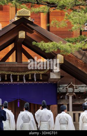 Shinto-Priester in weißen jōe-Gewändern und schwarzen Kanmuri-Kopfbedeckungen stehen vor dem großen Giebeldach über dem Eingang des Shinto-Schreins für zeremonielles Ritual. Stockfoto