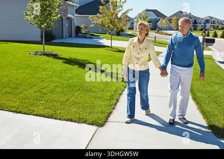 Hände halten, spazieren gehen und altes Paar in der Nachbarschaft für Wellness, frische Luft und aktiv am Morgen. Ruhestand, Ehe und glücklicher älterer Mann und Stockfoto