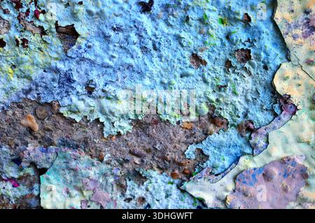 Eine Nahaufnahme einer Wand mit Schichten abblätternder Farbe in Blau- und Grüntönen. Die Textur ist rau und ungleichmäßig, mit Flecken aus freiliegendem Braun und Stockfoto