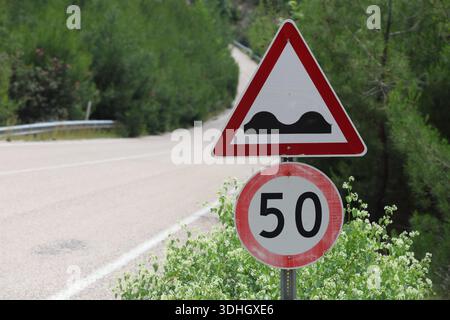 Europäische Geschwindigkeitsbegrenzung und unebene Straßenwarnschilder auf einer Landstraße mit 50 km/h Einschränkung und Sharp Chevron Curve Schild Stockfoto