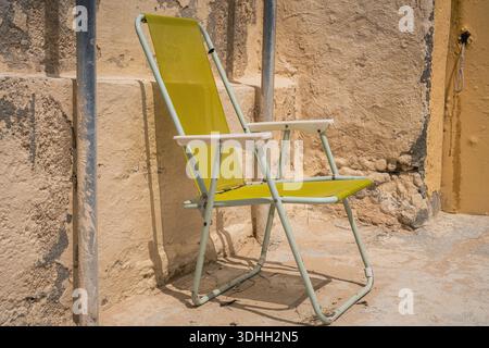 Ein einziger grüner Klappstuhl, der sich an eine raue Steinwand lehnt und Einfachheit, Stille und Spuren des täglichen Outdoor-Lebens festhält Stockfoto