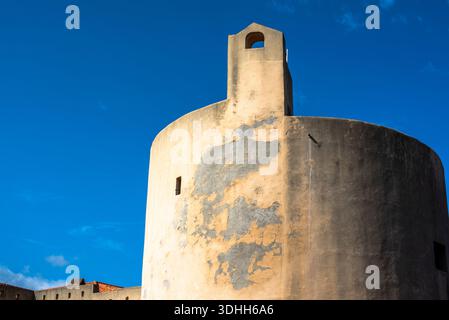 Runder historischer Turm mit verwitterter Putzfassade vor tiefblauem Himmel in Korsika, Frankreich. Minimalistische mediterrane Architektur, starke Geometrie, Sonne Stockfoto