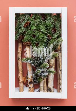 Dekorativer Holzrahmen mit Birkenstämmen und immergrünen Zweigen mit Tannenzapfen. Einrichtung. Weihnachts-Winterkarte. Rosafarbener Hintergrund Stockfoto