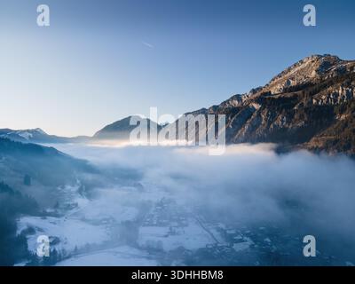 Aus der Vogelperspektive auf Berggipfel, die durch ein Meer aus ätherischem Nebel durchdringen, das Dorf liegt unter einer Schneedecke, Andelsbuch, Österreich. Stockfoto