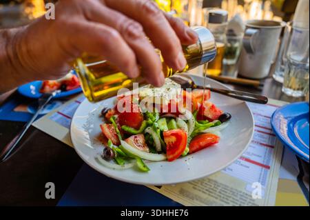 Traditioneller griechischer Salat mit Gemüse und Käse, handgegossenes Öl, voller Tisch mit Geschirr. Essen am Restauranttisch. Stockfoto