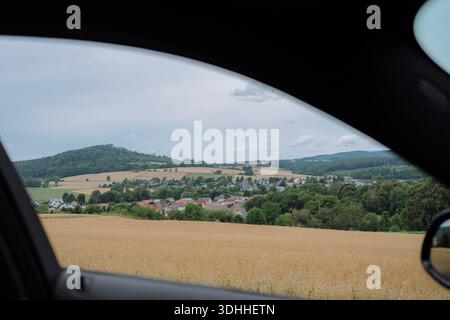 Sanfte Hügel und ein malerisches Dorf, das durch ein Autofenster betrachtet wird, unterstreichen die Schönheit der Landschaft auf einer friedlichen Fahrt. Die üppige Landschaft Stockfoto