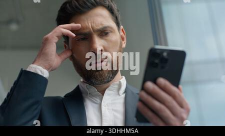 Schockiert verwirrt genervt kaukasischer männlicher Geschäftsmann Geschäftsmann im Büro, der Smartphone liest schlechte Nachrichten verärgert mit Handy frustriert Stockfoto