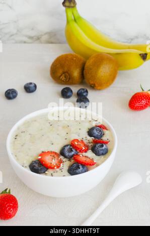 Eine köstliche Schüssel Bananen- und Kiwi-Smoothie, dekoriert mit frischen Beeren und Chiasamen. Eine helle Komposition eines gesunden Frühstücks auf einem hellen Rücken Stockfoto
