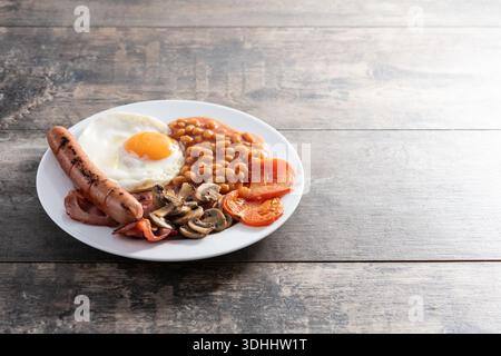 Komplettes englisches Frühstück mit Spiegelei, Speck, Würstchen und Bohnen auf Holztisch. Stockfoto