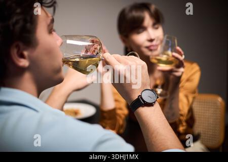 Junger kaukasischer Mann und junge kaukasische Frau, die zusammen sitzen und Wein trinken, sich unterhalten, beide Weingläser halten, konzentrieren sich auf den Mann im Vordergrund Stockfoto