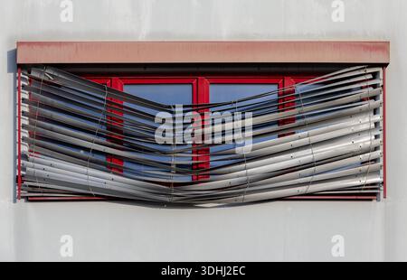 Reparaturen erforderlich - Rote Fenster mit defekten venezianischen Außenjalousien an der Fassade des Wohngebäudes Stockfoto