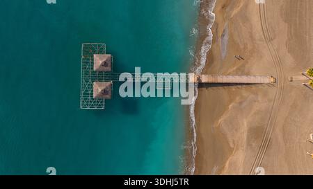 Die symmetrische vertikale Zugkraft eines modernen Holzpiers und Strohdächer über dem tiefblauen Meer. Ein ästhetischer Platz, der Luxusresorts und m Stockfoto