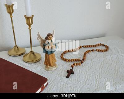 Katholische Ecke zu Hause. Engelsfigur, Rosenkranzperlen aus Holz, Kreuz und Gebetsbuch. Glaube, Symbole und Traditionen. Stockfoto