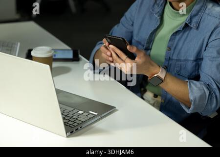 Erwachsene Frau hält Telefon auf weißem Schreibtisch im Büro, silberner Laptop neben Kaffeetasse und Tablet. Technologie, Produktivität, Arbeitsplatz, modern, Unternehmen, Kommunikation, minimalistisch || Modell veröffentlicht Stockfoto