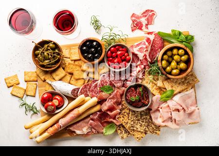 Vorspeisen mit verschiedenen Antipasti, Wurstwaren, Snacks und Rotwein auf weißem Hintergrund. Wurst, Schinken, Tapas, Oliven und Cracker für eine Buffetparty. Draufsicht, flach liegend Stockfoto