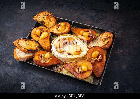 Im Ofen gebackener Camembert-Käse mit karamelisierten glasierten Birnen, Walnüssen und Trauben sowie Baguette auf rustikalem Metallteller Stockfoto