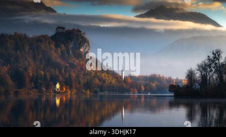 Aus der Vogelperspektive des Bleder Sees spiegelt die Burg auf einer Klippe wider, Herbstfarben malen die Landschaft unter einem nebeligen Himmel, Spodnja Lua, kofja Loka, SL Stockfoto