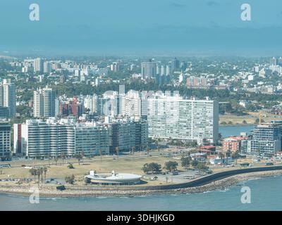 Blick aus der Vogelperspektive auf die Küste mit ihren markanten Gebäuden und lebhaften Grünflächen im Kontrast zum tiefblauen Meer, Montevideo, Departamento d Stockfoto