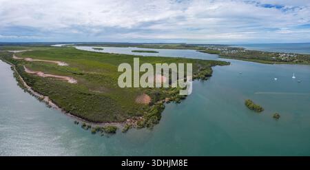 Aus der Vogelperspektive auf den Serpentinfluss, der sich durch grüne Mangroven schlängelt und unter einem bewölkten Himmel auf das braune Meer trifft, River Heads, Queensland, Australien Stockfoto