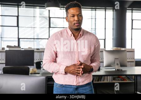Afroamerikanischer Mann, der mit gefesselten Händen in einem modernen Büro steht und rosa Hemd neben Monitoren trägt Stockfoto
