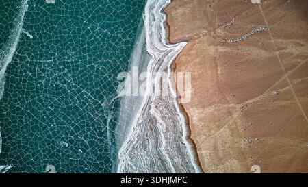 Aus der Vogelperspektive auf dem See mit gefrorenem Ufer und braunem Land. Abstrakter Natur-Hintergrund mit einzigartiger Wintertextur. Stockfoto
