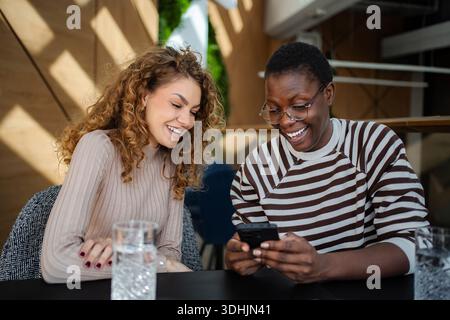 Freundinnen lachen mit Smartphone im Café Stockfoto