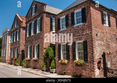 Eine Reihe historischer Häuser aus rotem Backstein mit schwarzen Fensterläden entlang eines Gehwegs in Charleston. Stockfoto