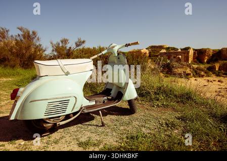 Ein grüner Roller parkt am Rande einer Feldstraße. Der Roller ist alt und hat einen weißen Sitz. Die Szene ist ruhig und friedlich, mit dem Roller Stockfoto