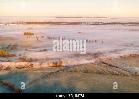 Aus der Vogelperspektive sehen Sie goldenes Sonnenlicht, das die nebeligen Felder und die alten Wittenham-Klumpen küsst, die eine ruhige Landschaft schaffen, Wittenham-Klumpen, Oxfordshire, Engl Stockfoto