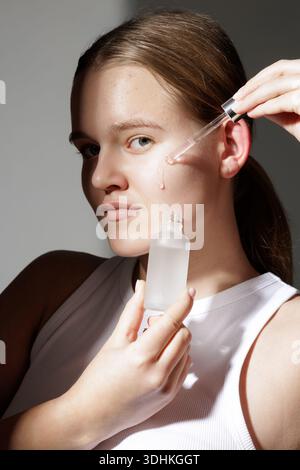 Vertikales Atelierporträt einer jungen Frau, die Serum mit Tropfer aufträgt, mit Flecken und Rötungen. Geeignet für Hautpflege Website Banner oder Social Adv Stockfoto