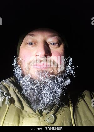 Nahaufnahme eines Mannes mit einem gefrorenen Bart, bedeckt mit Raureif und Eis. Überlebenskonzept für extreme Kälte Stockfoto