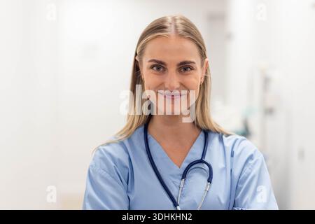 Frau in hellblauen Schutten, die mit gekreuzten Armen im medizinischen Flur steht und Stethoskop trägt Stockfoto