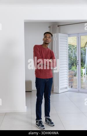 Afroamerikaner mit rotem Pullover, zu Hause mit überkreuzten Armen in der Nähe der Schiebetür Stockfoto