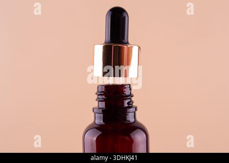 Öliger Tropfen tropft aus der Pipette in die Kosmetikflasche, isoliert auf beigefarbenem Hintergrund. Stockfoto