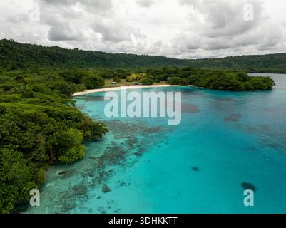 Aus der Vogelperspektive auf das ruhige türkisfarbene Wasser, das die pulsierende grüne Küste unter einem ruhigen Himmel umschließt, Espiritu Santo, Provinz Sanma, Vanuatu. Stockfoto