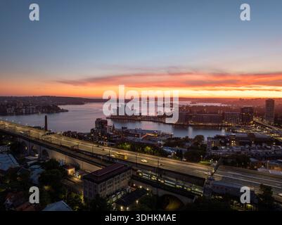 Blick aus der Vogelperspektive auf das berühmte Opernhaus von Sydney, das den feurigen Sonnenuntergang über dem ruhigen Hafen reflektiert, eingerahmt vom Stahlbogen der Harbour Bridge, Sydney Stockfoto