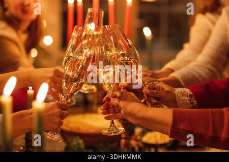 Freunde stoßen fröhlich mit Sektgläsern in gemütlicher Atmosphäre an, beleuchtet von Kerzen und festlicher Einrichtung, um die Essenz des Feierns und To festzuhalten Stockfoto