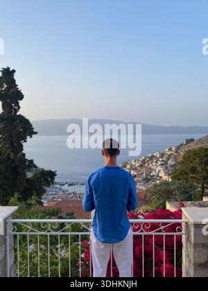 Rückansicht eines Mannes auf einem Balkon mit Blick auf eine Küstenstadt und Bucht zur goldenen Stunde. Stockfoto