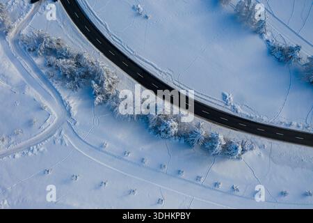 Aus der Vogelperspektive einer dunklen Bandstraße, die durch eine unberührte weiße Schneelandschaft verläuft, umgeben von Bäumen, die in zartem, eisigem Filigran vereist sind, Bergün Filisur, GRI Stockfoto