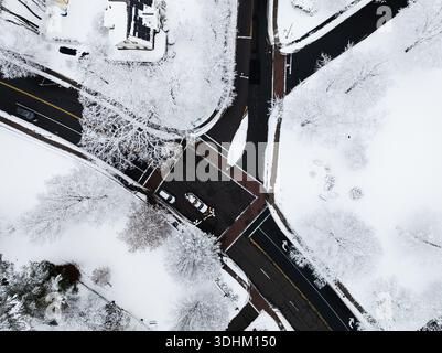 Aus der Vogelperspektive mit Blick auf eine verschneite Kreuzung mit dunklem Asphalt, die die weiße Landschaft durchquert und von oben auf schneebedeckte Bäume. Welles Stockfoto